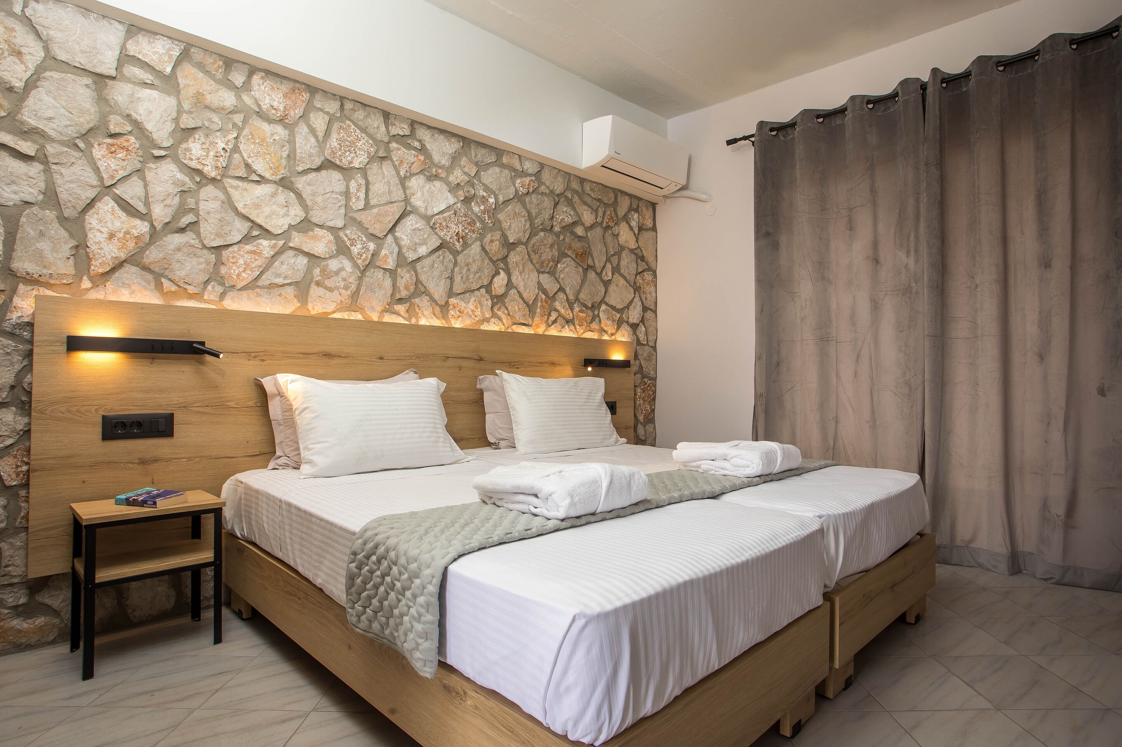 A double bed with a wooden headboard, a nightstand, and a stone wall.
