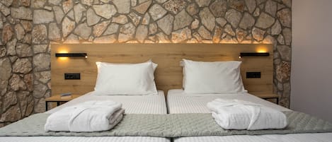 A double bed with white linens and two pillows, a stone wall behind, and a wooden headboard with two bedside tables.