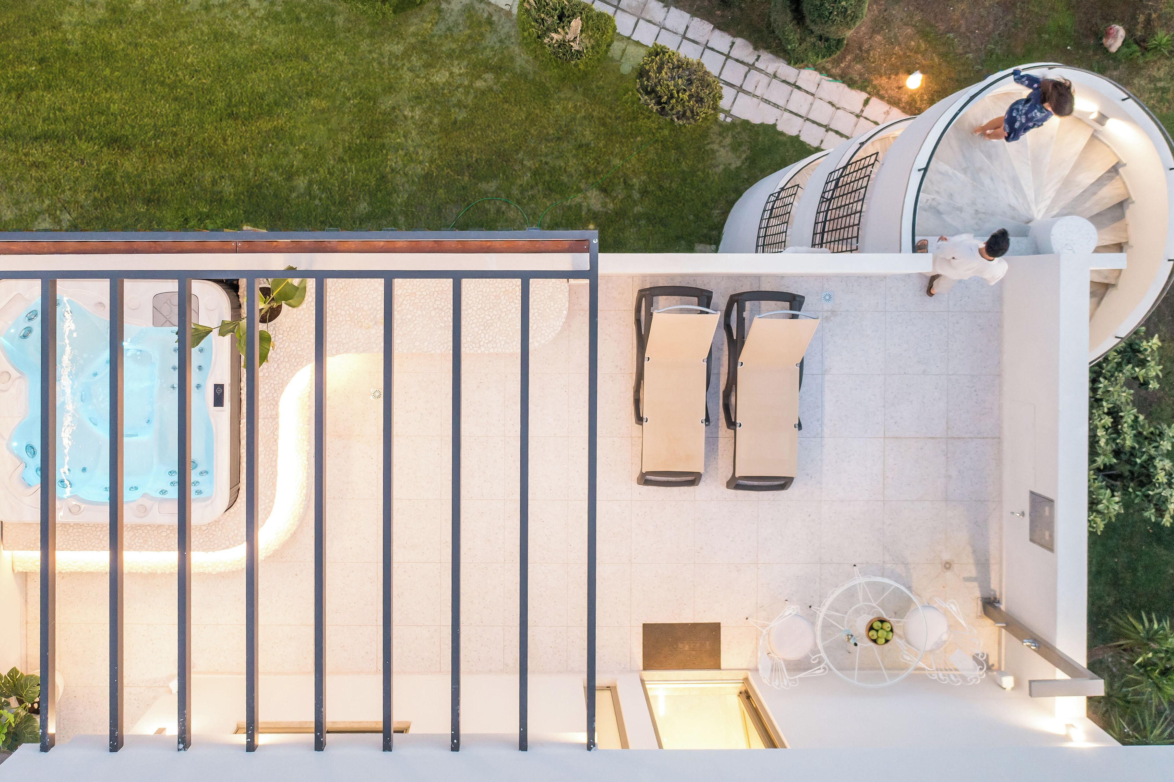 A modern outdoor bathroom with a hot tub, two sun loungers, and a small seating area with a bicycle wheel design.