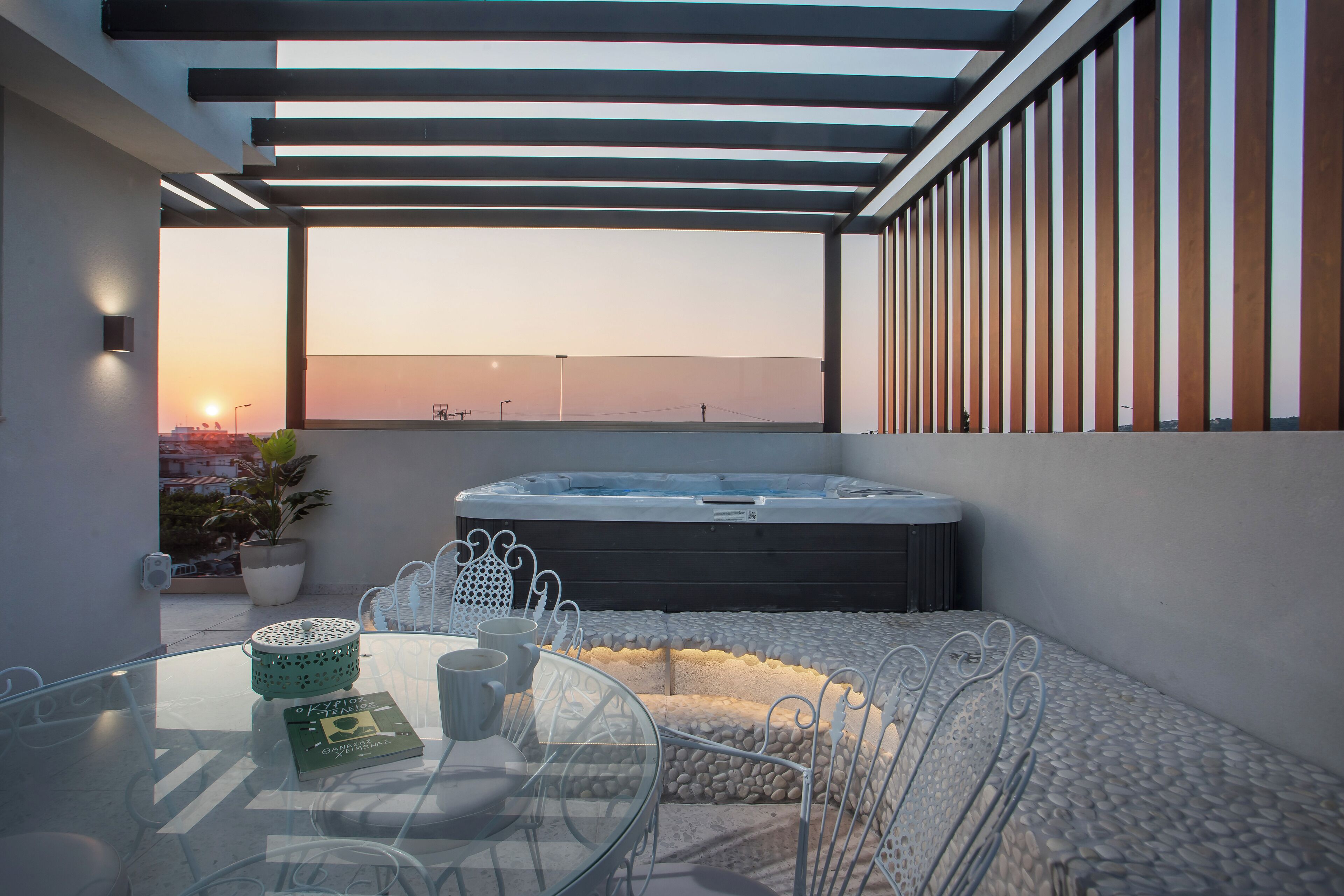 A glass table with chairs and a hot tub on a balcony with a view of the sunset.
