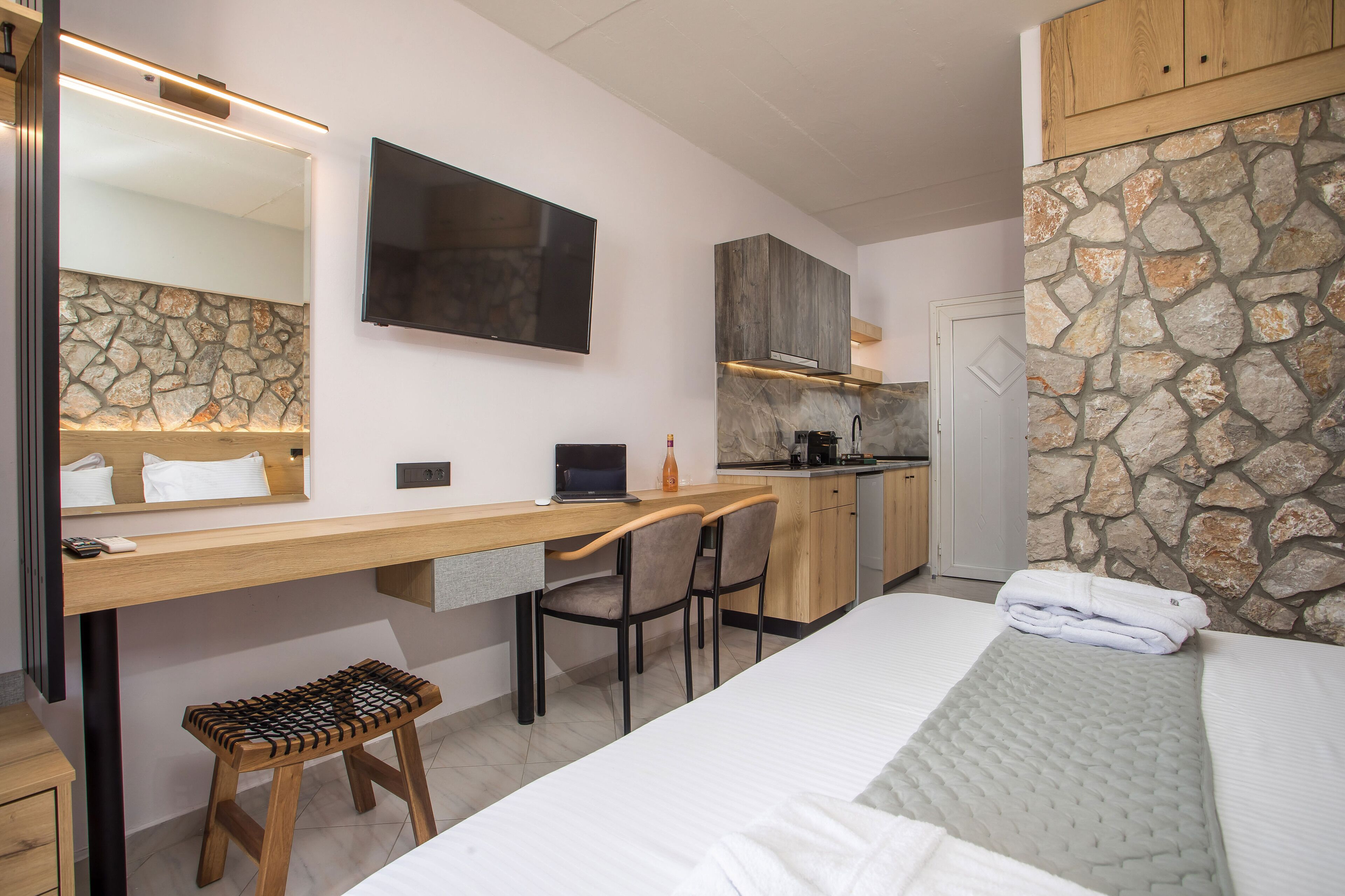 Habitación de hotel pequeña con cama, escritorio con una laptop, silla, taburete, televisor y kitchenette.