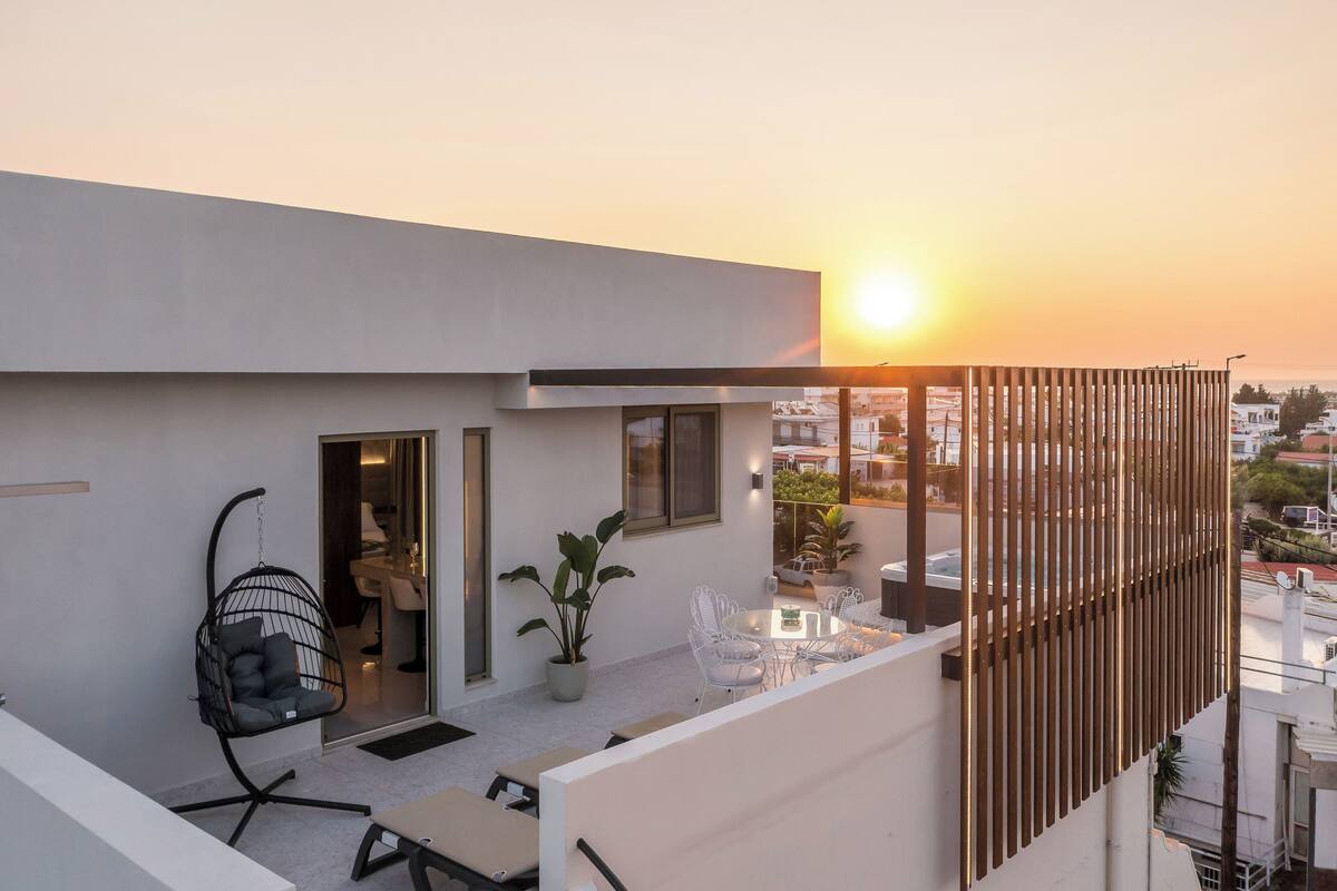 A modern balcony with a hanging chair, a dining table with chairs, and a potted plant.