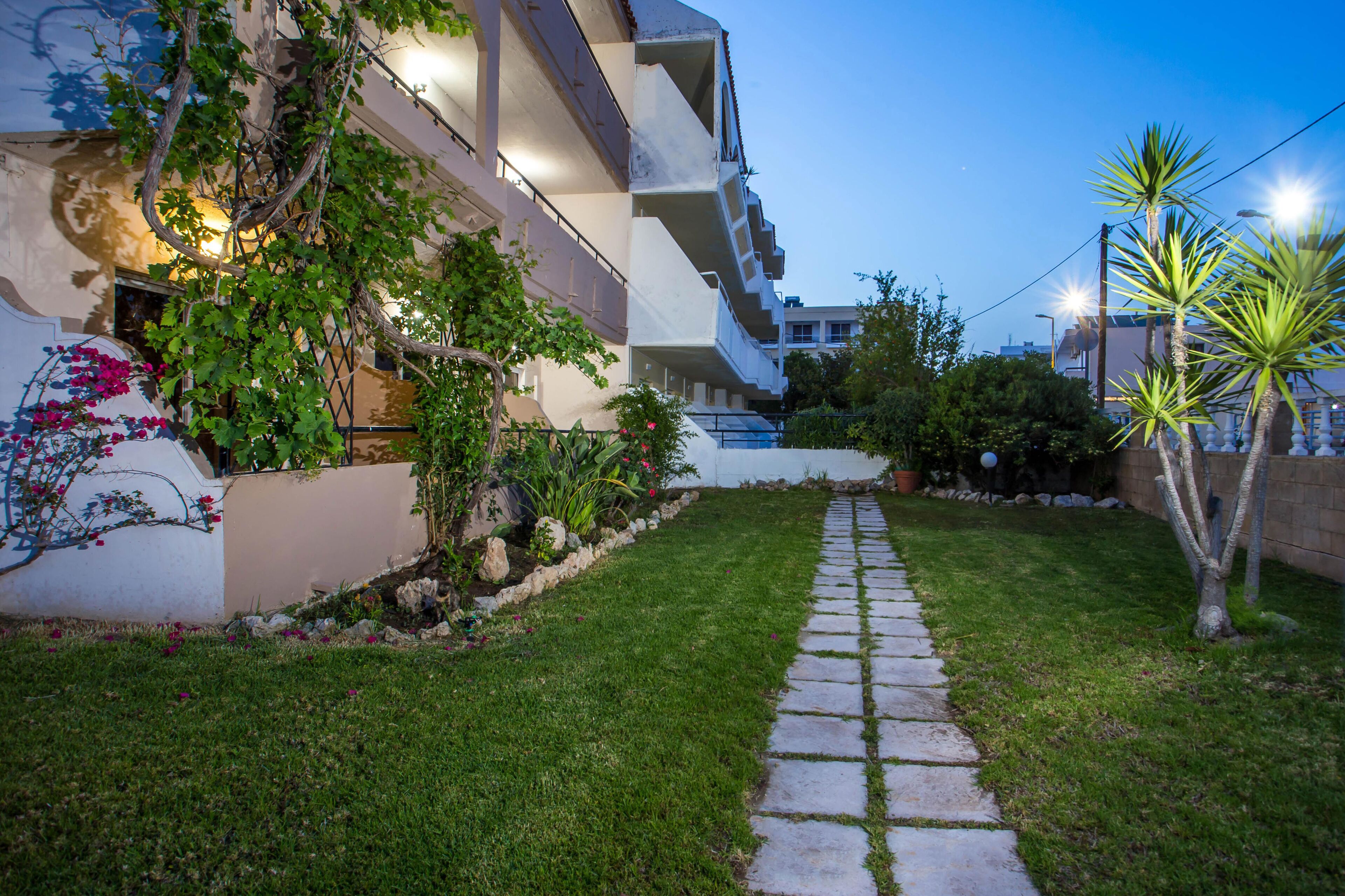 Un sendero que lleva a un edificio con jardín y una palmera.