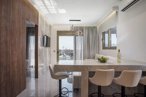 A modern kitchen with a marble countertop, a dining area with bar stools, and a view of the city through large windows.