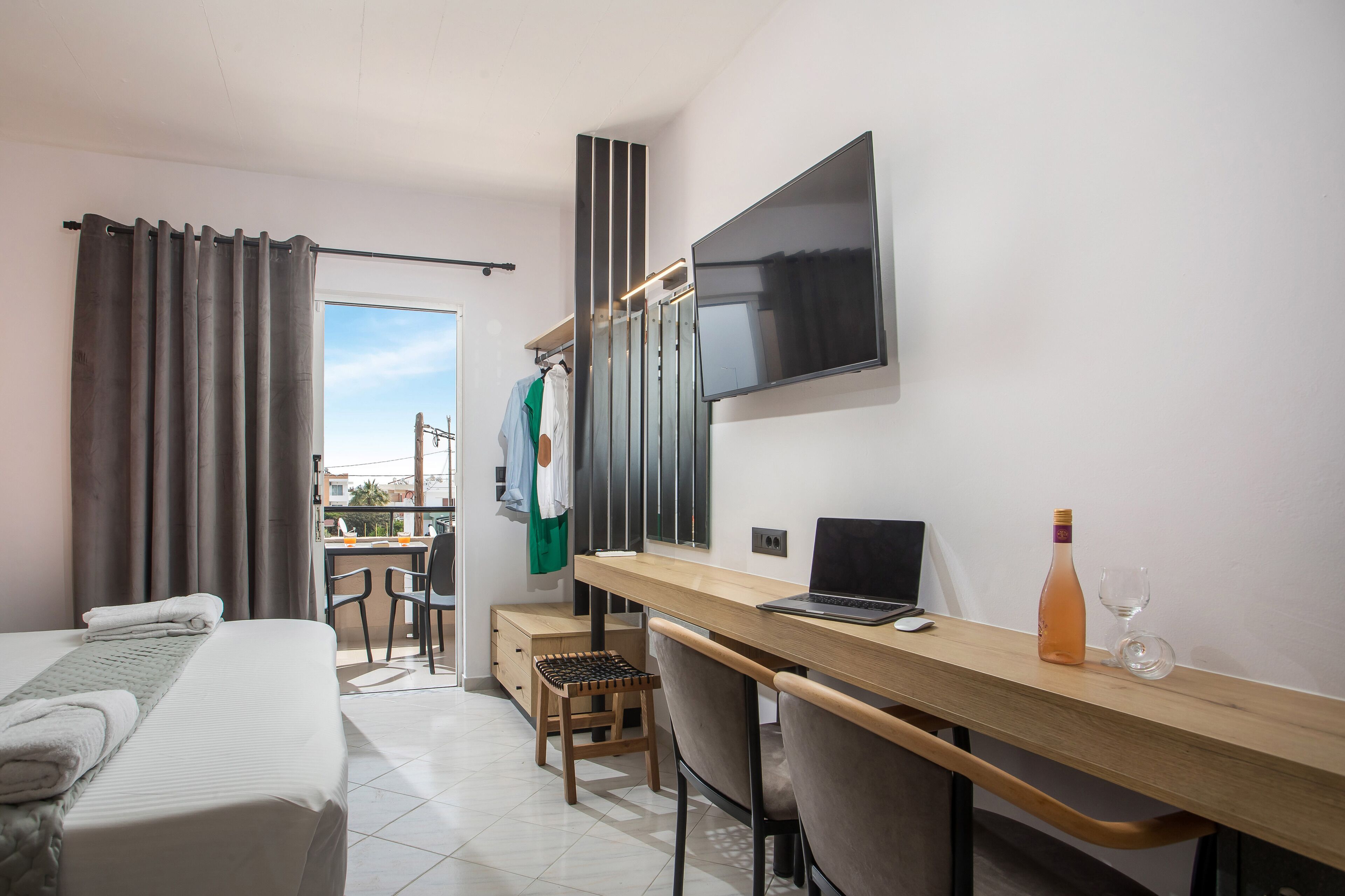 Habitación de hotel con cama, escritorio con una computadora portátil, televisor y balcón con mesa y sillas.