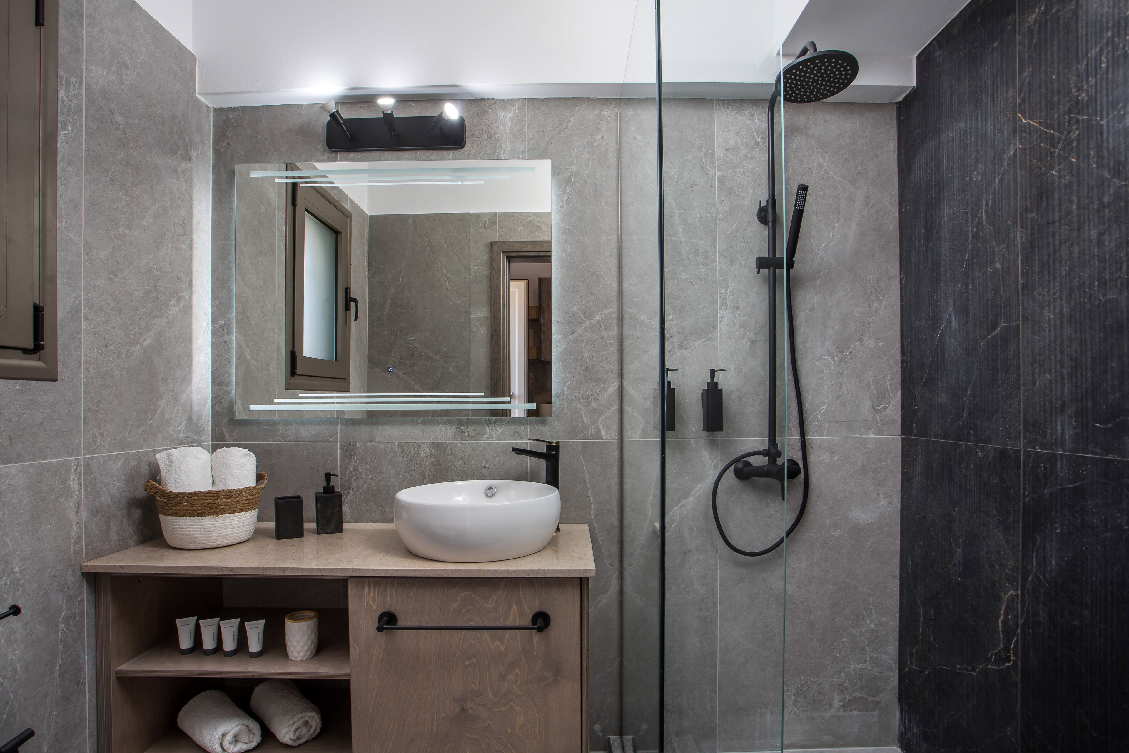 A modern bathroom with a large mirror, a white sink, and a glass-enclosed shower.