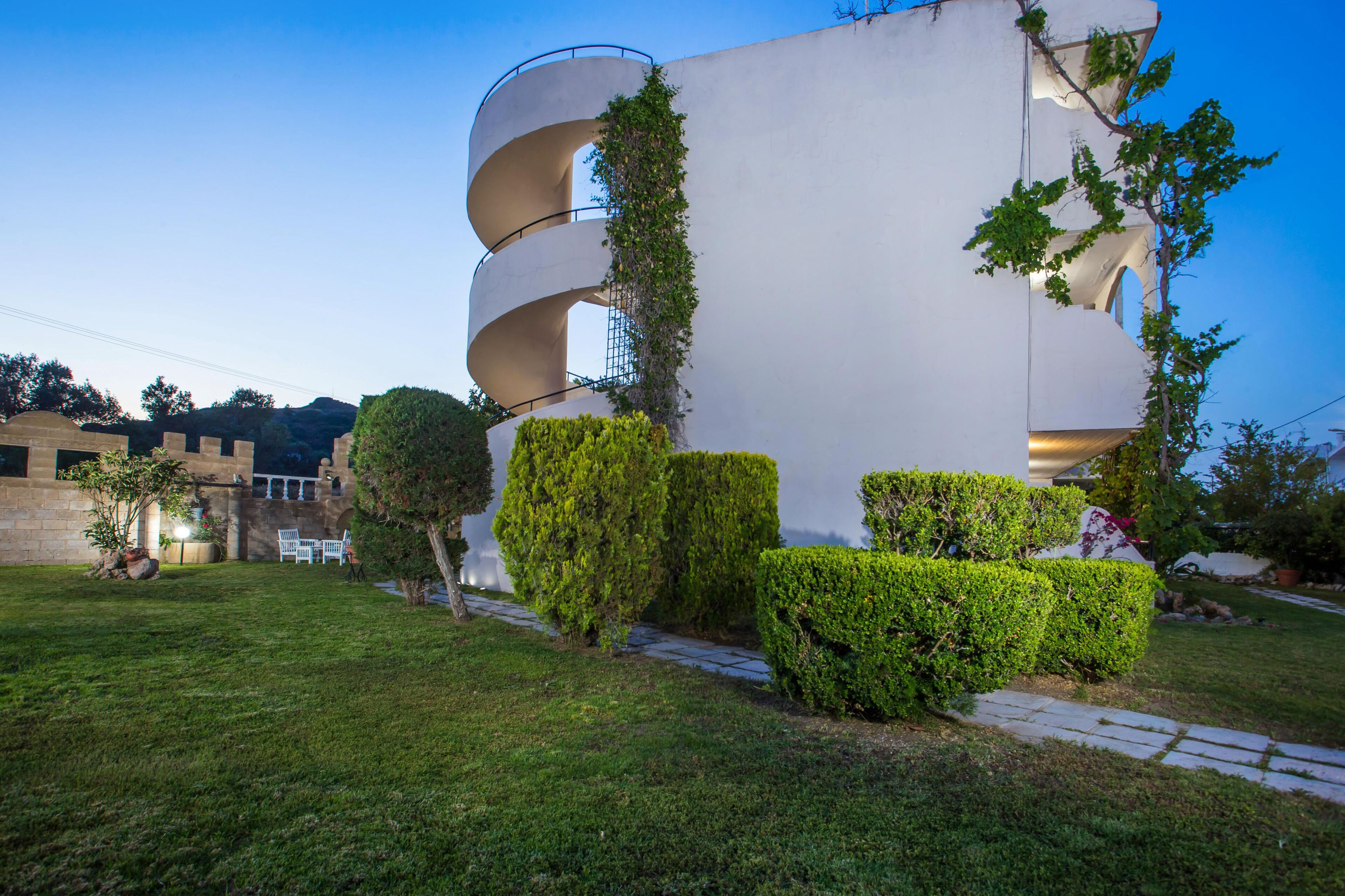 Un edificio moderno con un design a spirale originale, circondato da siepi curate e un viale in pietra.