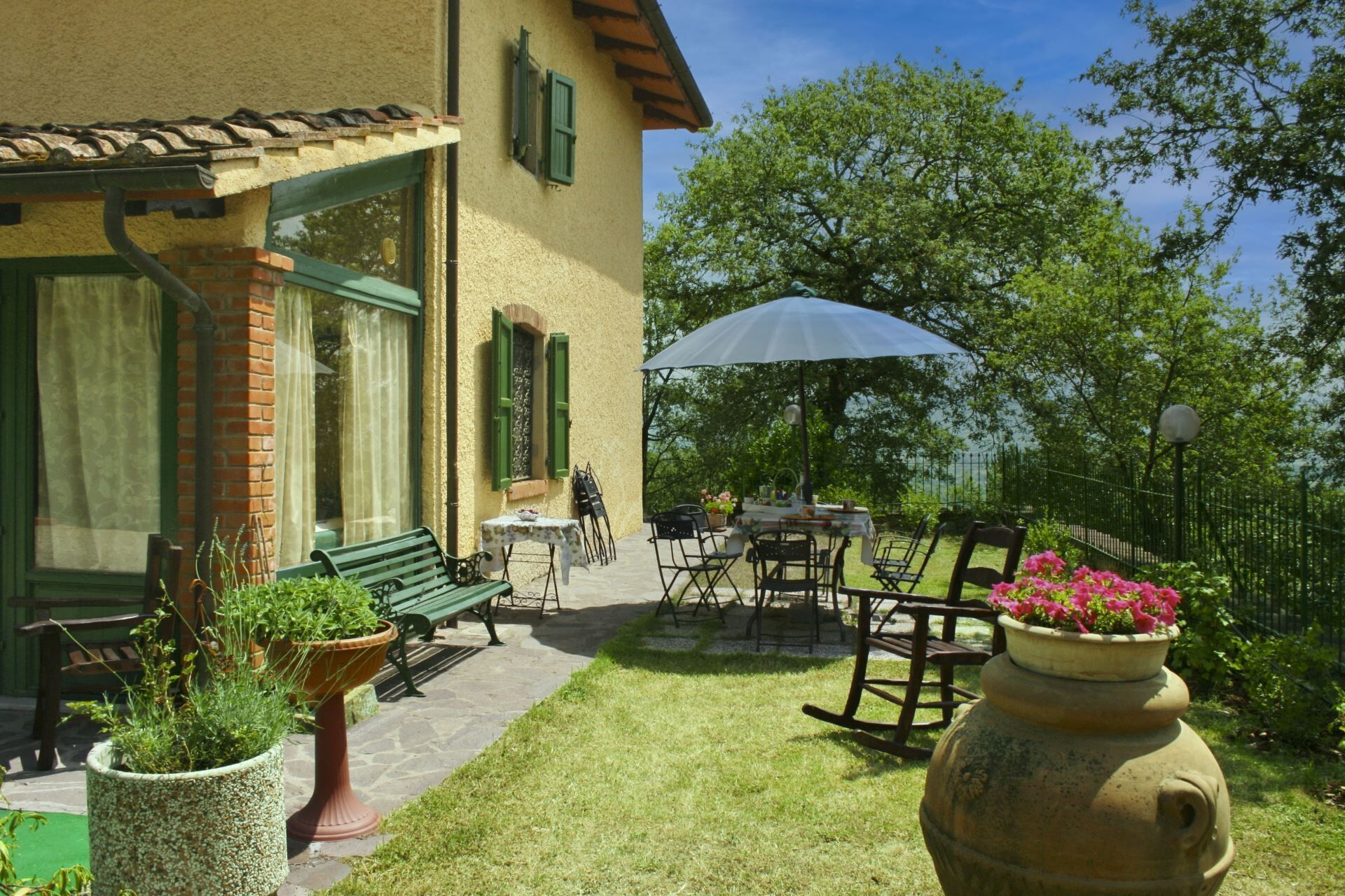 Une terrasse avec des meubles d’extérieur, une table recouverte d’une nappe blanche et un grand pot de fleurs.