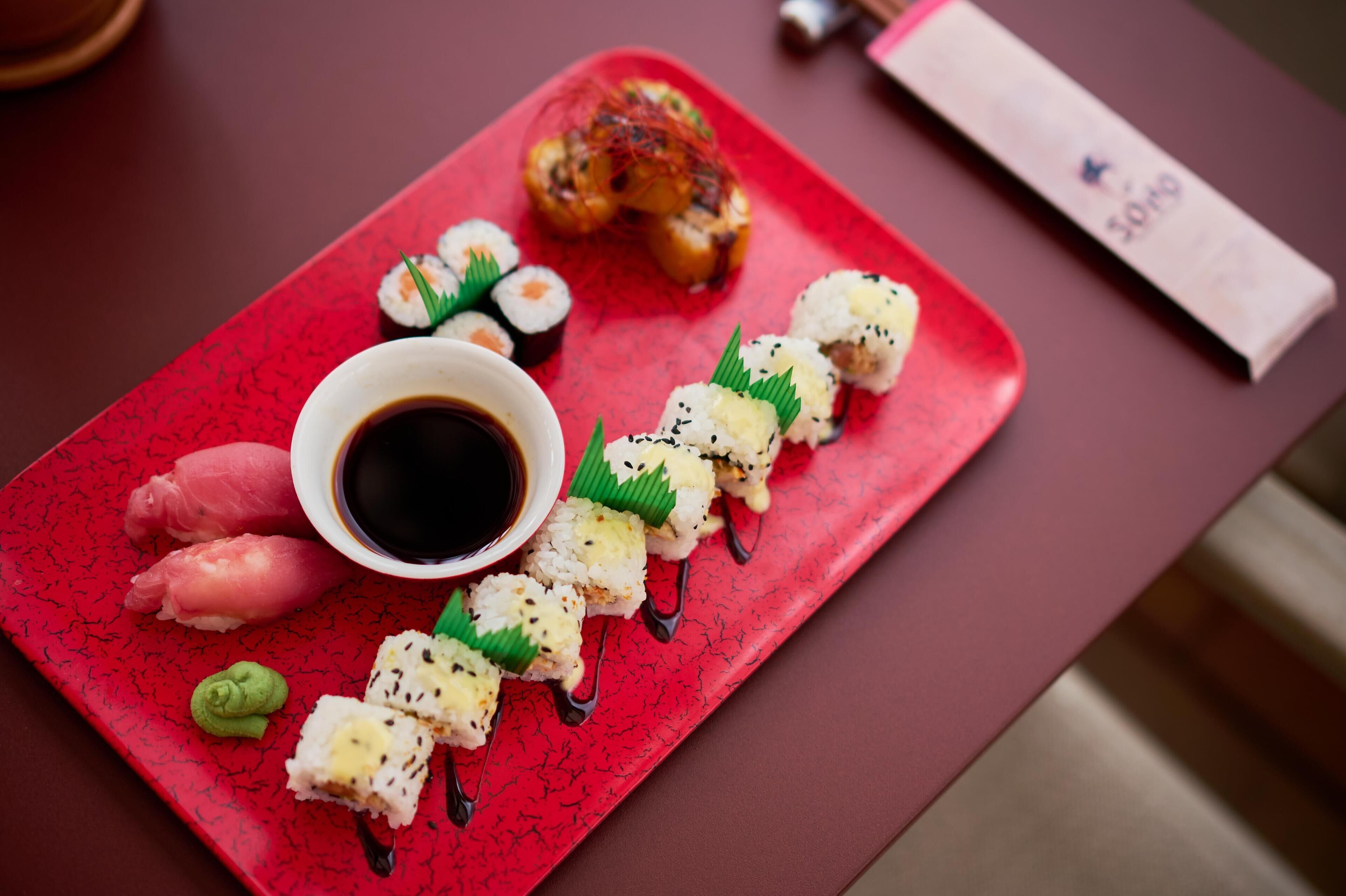 Ein rotes Tablett mit Sushi, einer kleinen Sojasaucenschale und einer Speisekarte.