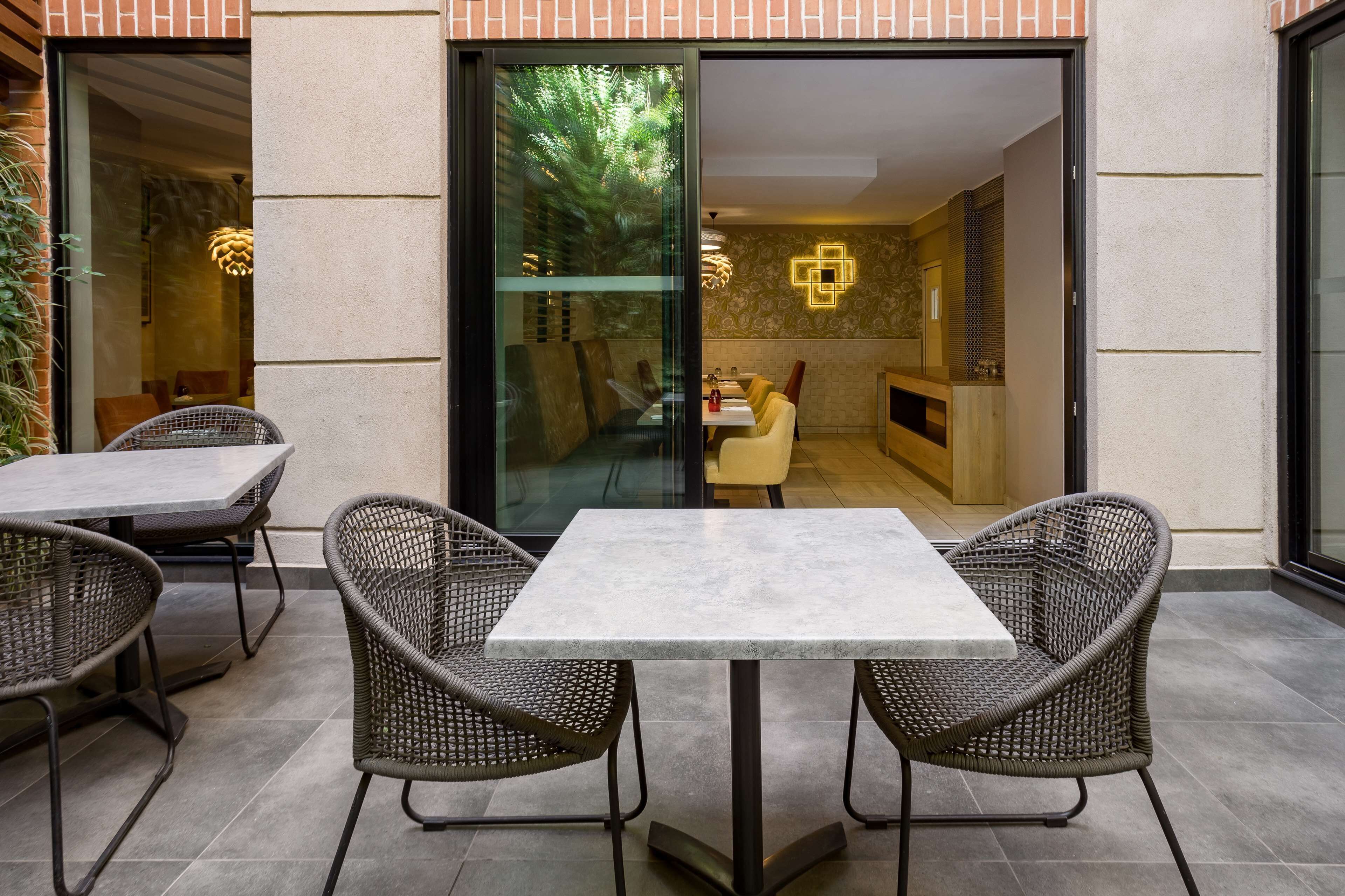 Un espace patio extérieur avec une table et des chaises, une porte vitrée donnant sur l’intérieur et un mur orné de motifs.
