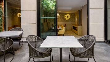 An outdoor patio area with a table and chairs, a glass door leading inside, and a patterned wall.