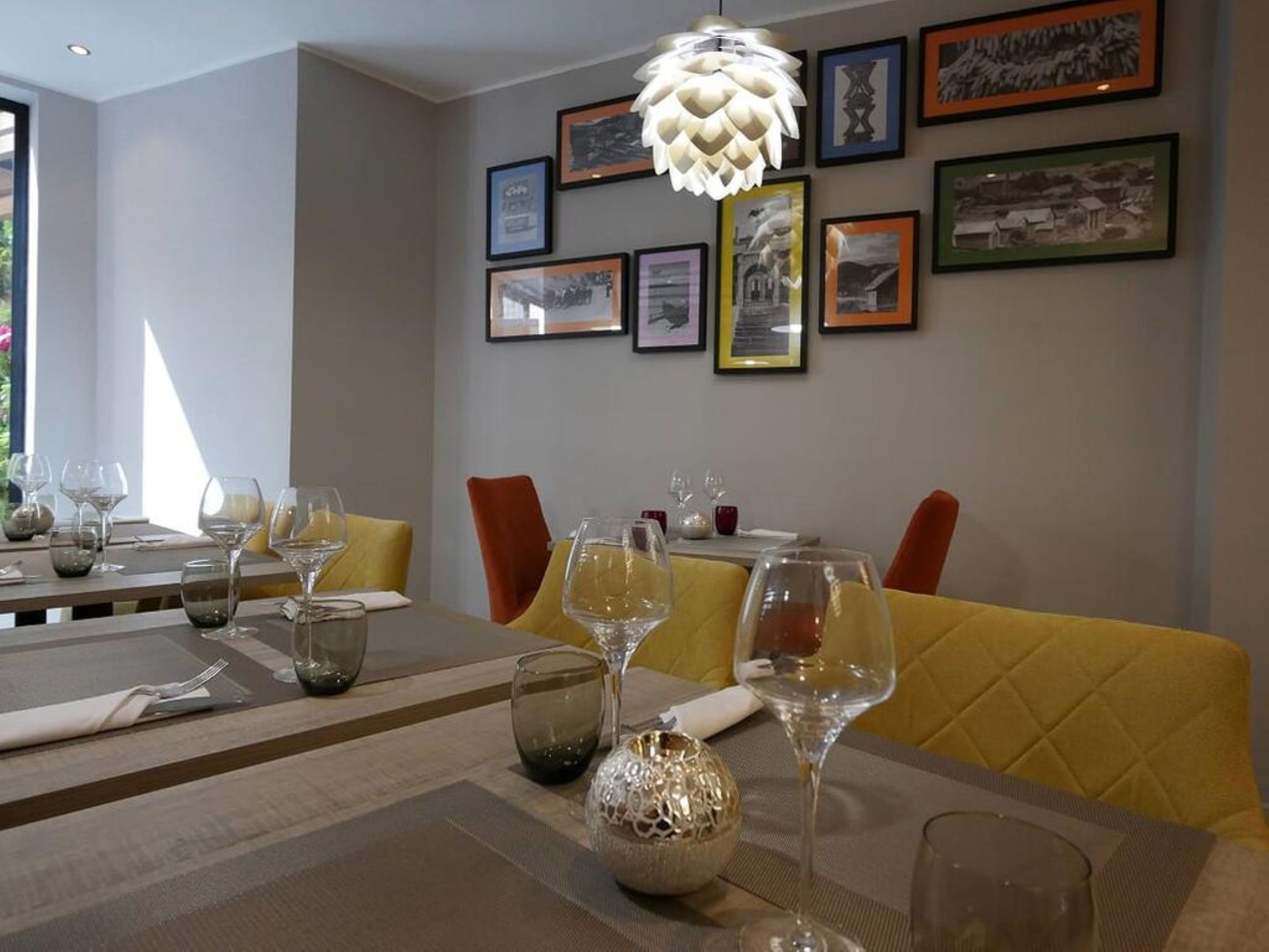 A dining area with tables set for two, featuring yellow upholstered chairs and a variety of wine glasses and water glasses on the tables.
