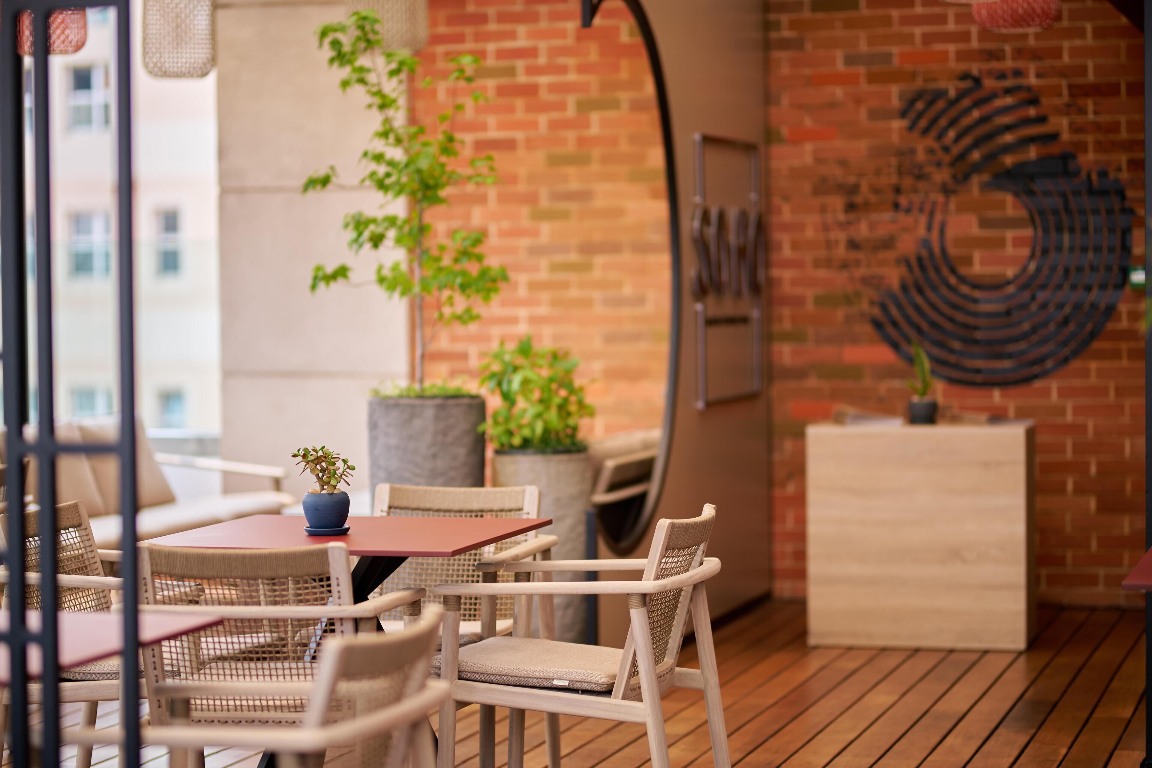 A cozy outdoor seating area with wicker chairs and a table, a potted plant, and a brick wall with a metal sculpture.