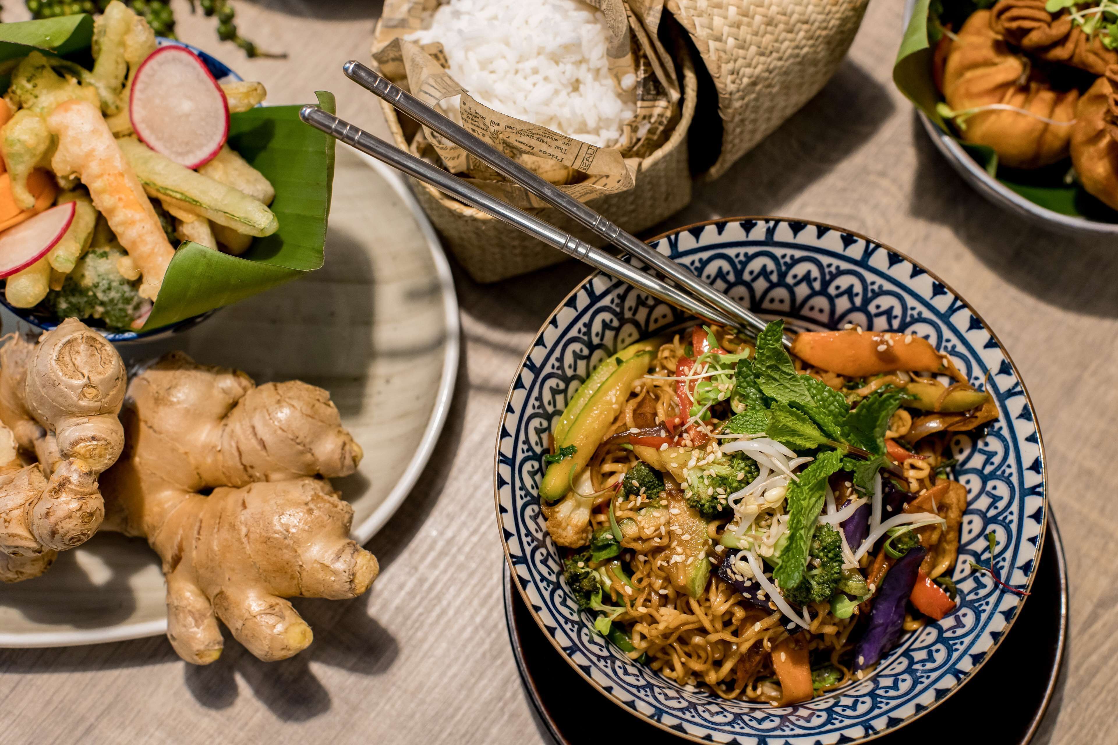 A table with a bowl of noodles, a basket of rice, and a plate of vegetables.