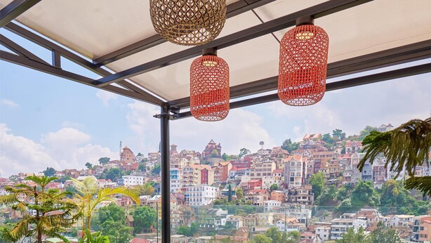 A covered outdoor seating area with a sofa, chairs, and a table, overlooking a cityscape. - Radisson Serviced Apartments Antananarivo City Centre (Antananarivo)