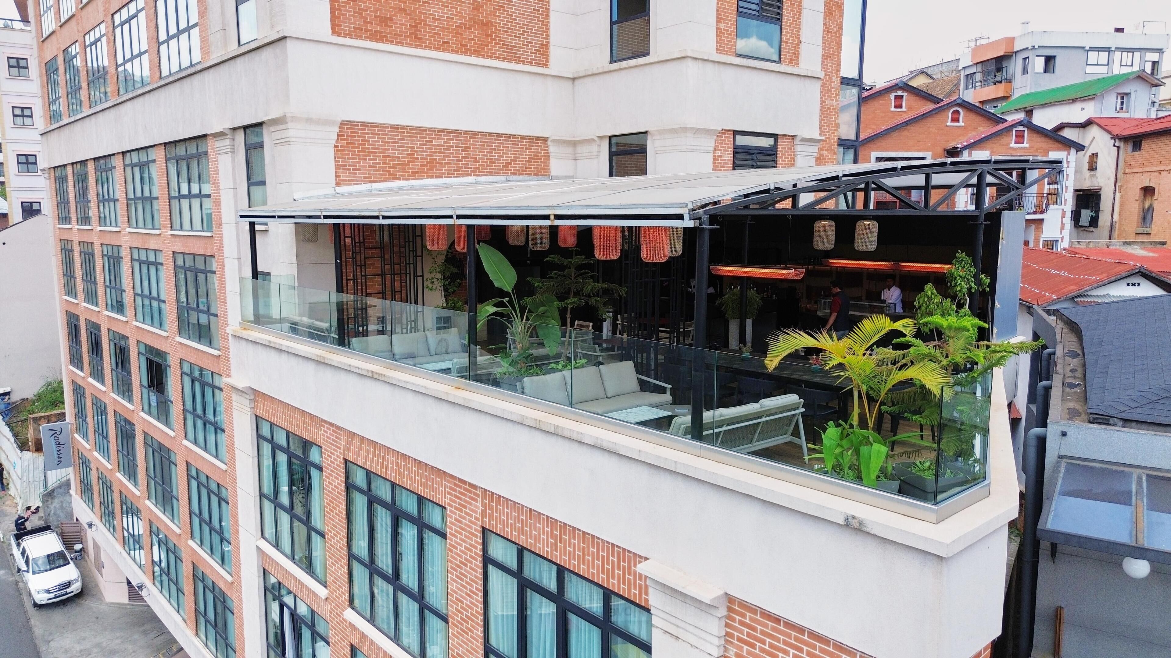 A modern building with a glass balcony area featuring outdoor seating and potted plants.