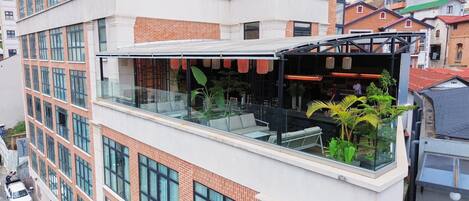 A modern building with a glass balcony area featuring outdoor seating and potted plants.