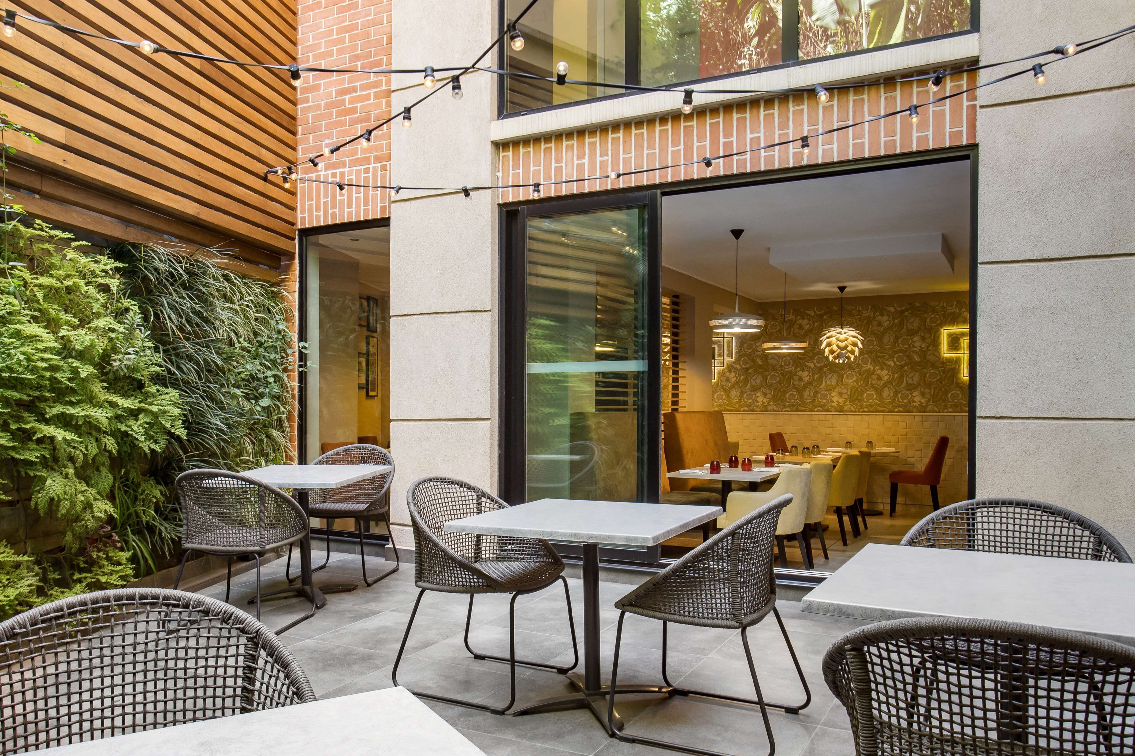 An outdoor patio with wicker tables and chairs, a brick wall, and a glass door leading to an interior dining area.