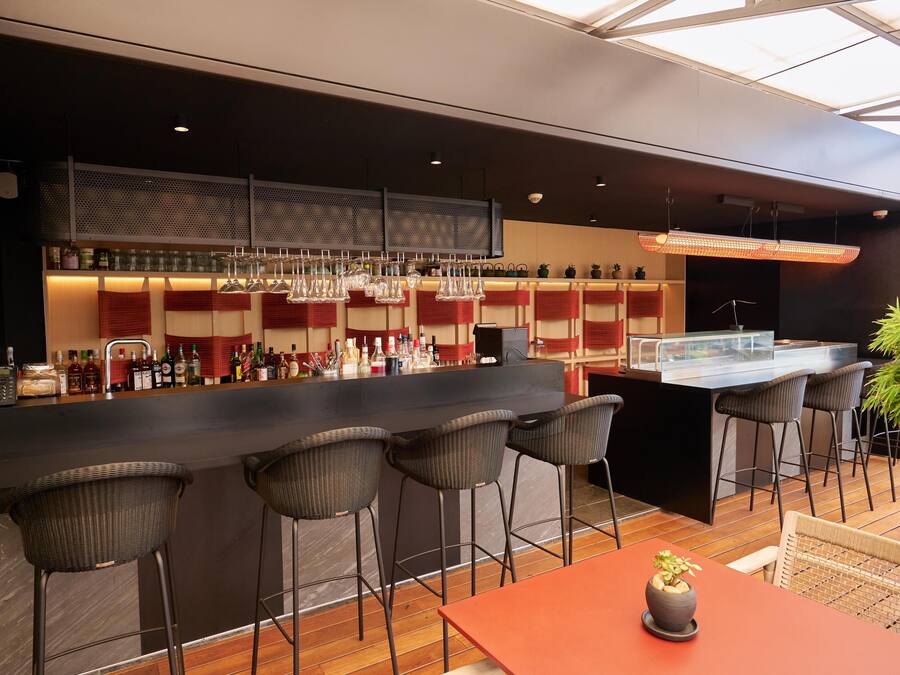 Un espace bar moderne avec un comptoir noir, des tabourets de bar en osier et une variété de bouteilles et de verres.