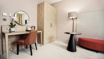 Una habitación de hotel moderna con un escritorio de madera, una silla, un sofá rojo, un espejo redondo, una lámpara y un armario.