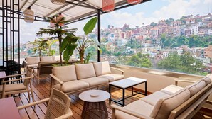 A terrace with wicker furniture, a round table, and a view of a cityscape. - Radisson Serviced Apartments Antananarivo City Centre (Antananarivo)