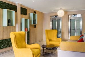 Un moderno vestíbulo con sillones amarillos, una mesa de centro de vidrio y una pared verde con un diseño texturizado.