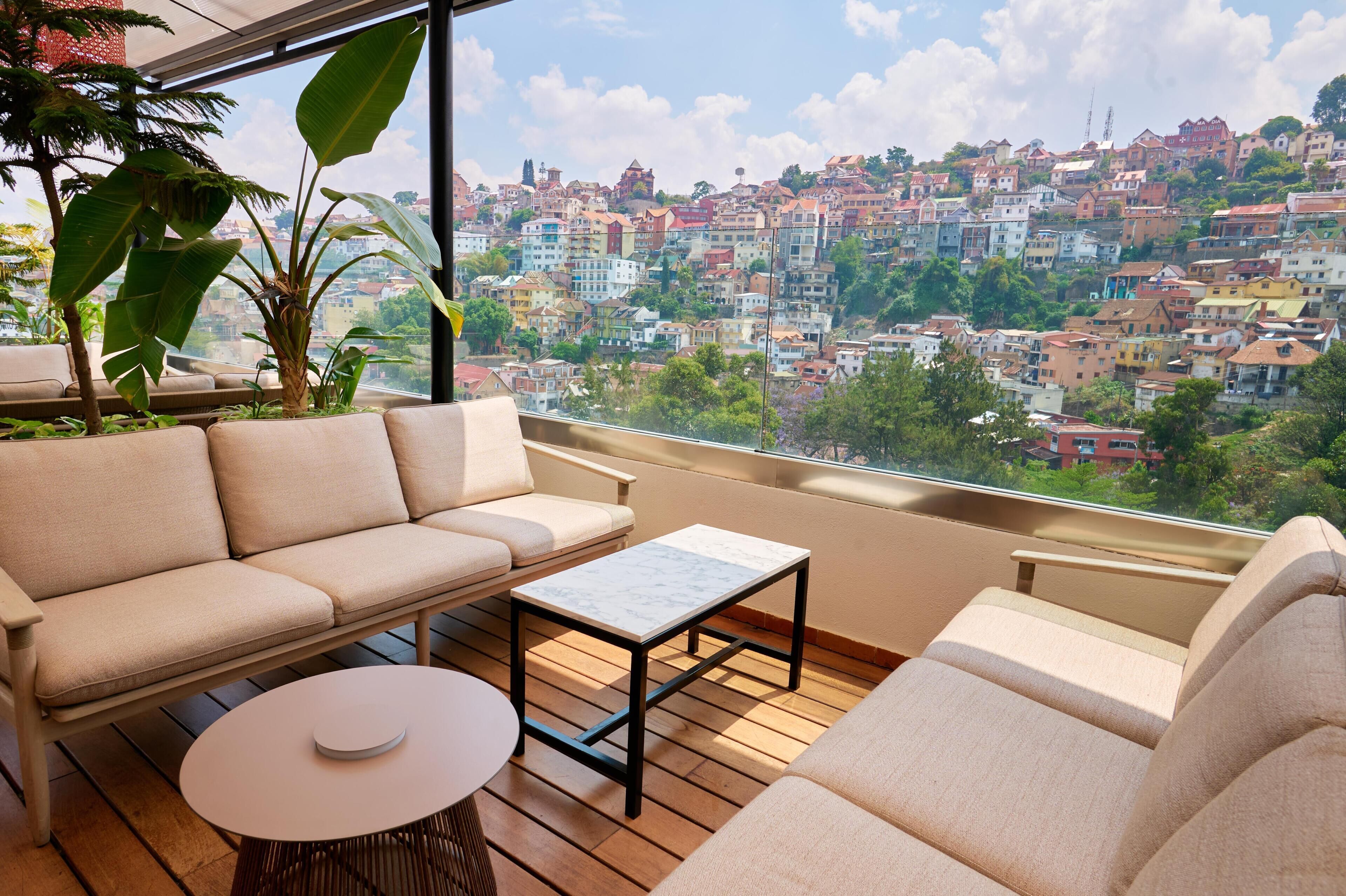 A balcony with a sofa, a small table, and a view of a colorful hillside town.
