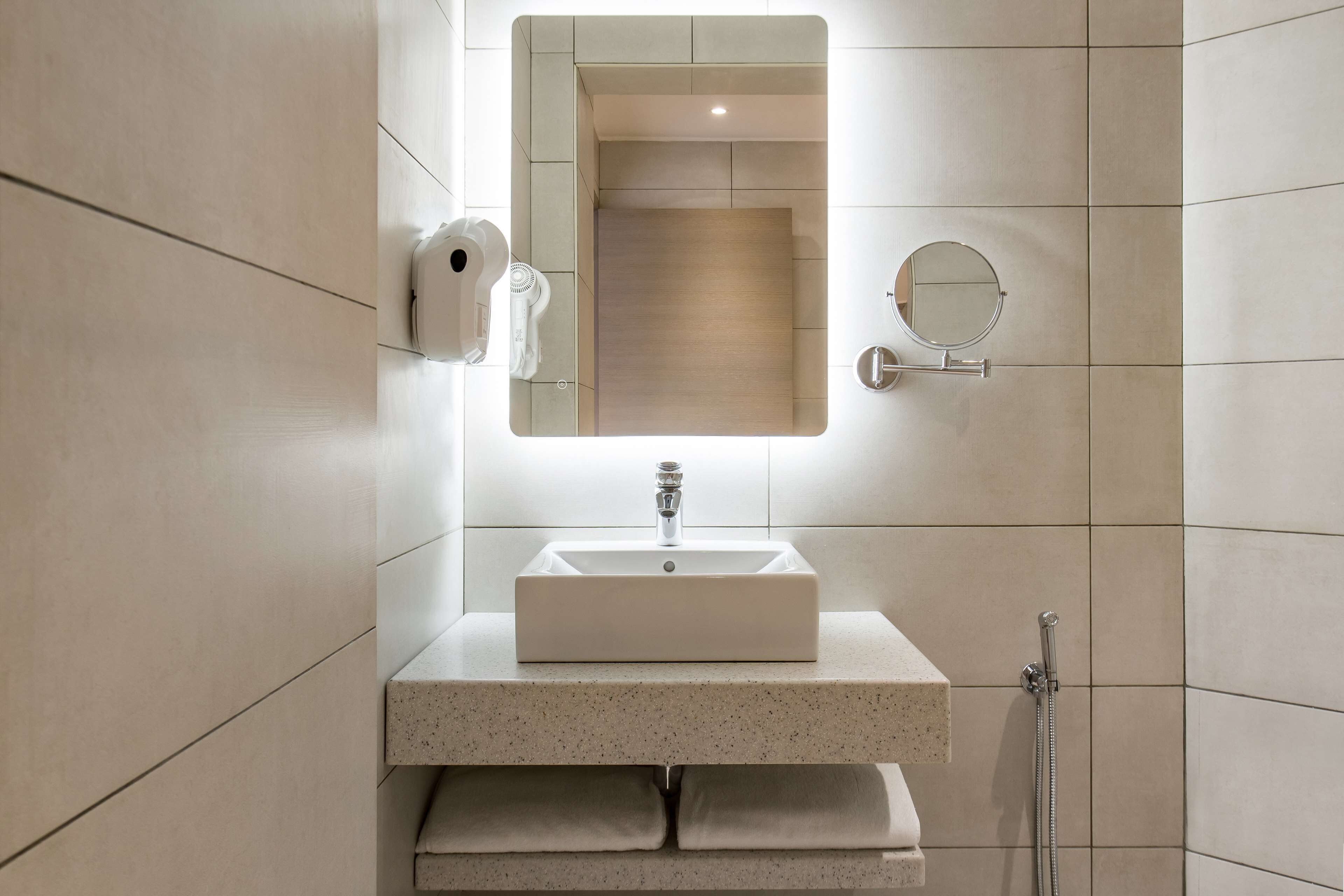 A bathroom with a rectangular sink, a mirror, a towel rack, and a handheld showerhead.