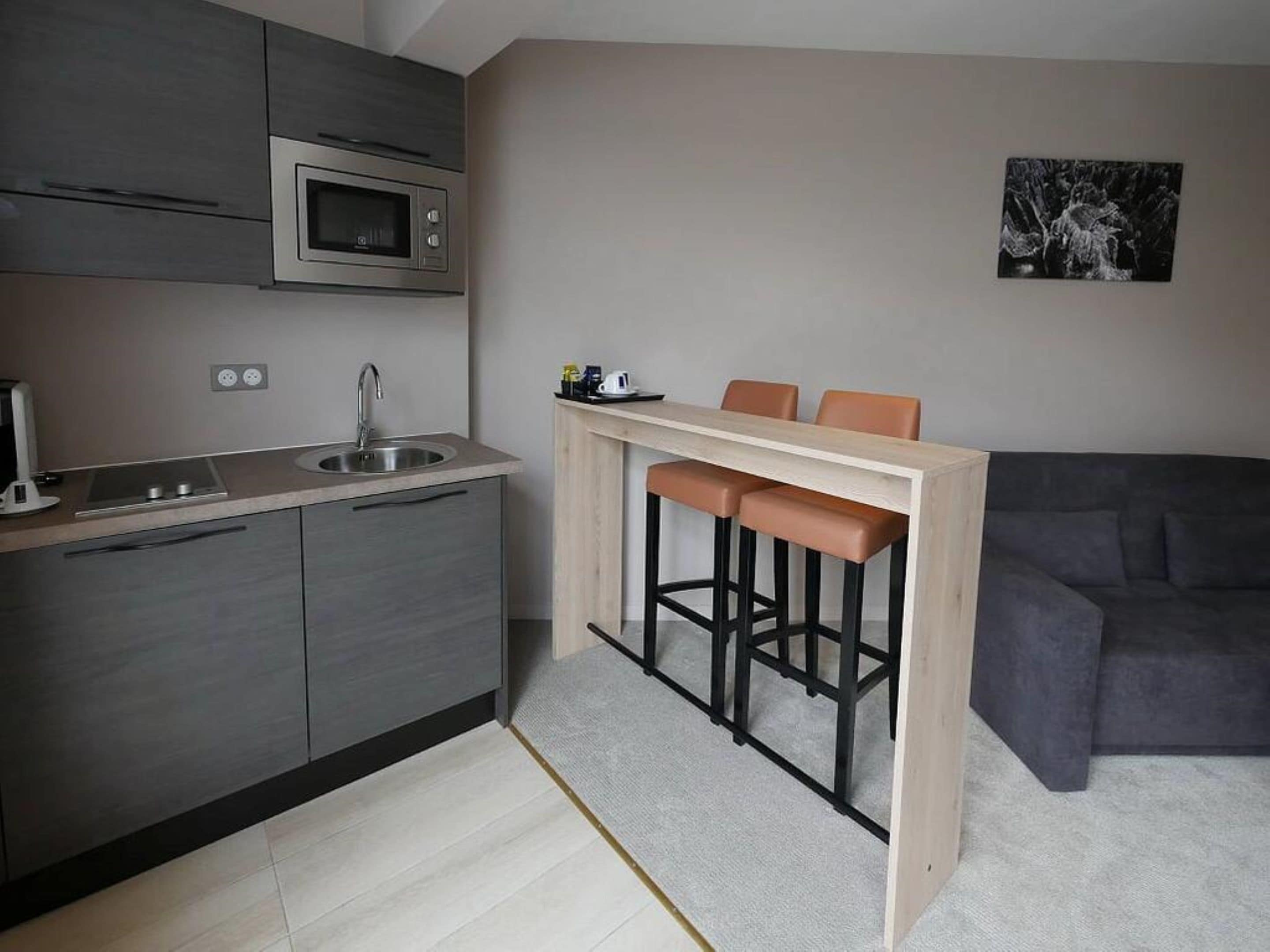 A compact kitchen with a microwave, sink, and modern cabinetry. There is a small bar area with stools and a couch in the living space.