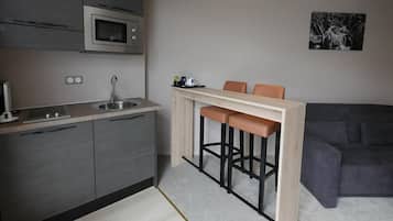 A compact kitchen with a microwave, sink, and modern cabinetry. There is a small bar area with stools and a couch in the living space.
