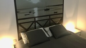 Een slaapkamer met een bed, kussens en een wanddecoratie van een rustige zee met boten.