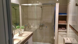 Een moderne badkamer met een douche met glazen wand, een wastafel met twee kommen en een toilet.