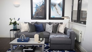 A modern living room with a grey sectional sofa, a coffee table, and decorative items. There are two abstract paintings on the wall, a floor lamp, and a vase with flowers on a side table.