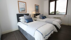 A hotel room with two beds, a nightstand, a lamp, and framed pictures on the wall.