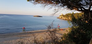 A beach with a lifeguard tower, a small island, and a cliff with a tower.