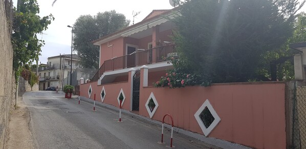 A residential building with a balcony, a red wall with diamond-shaped windows, and a street with bollards. - Apartment in Offers (Marina di Camerota)