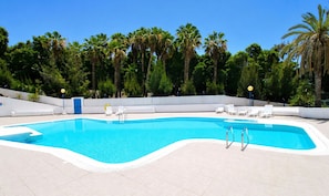 Une piscine rectangulaire bordĂ©e de blanc, entourĂ©e de chaises longues blanches et dâun mur blanc.