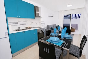 Une cuisine moderne avec des meubles bleus, une table Ă manger noire agrĂ©mentĂ©e dâassiettes bleues, et un canapĂ© gris dans lâespace salon.