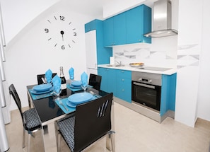 A modern kitchen with blue cabinets, a stainless steel oven, and a wall clock.