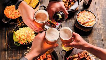 A group of people toasting with beer glasses, surrounded by various dishes and a bottle on a wooden table.