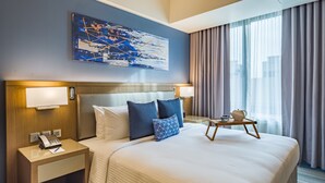 A hotel room with a large bed, two bedside tables, a telephone, a lamp, and a painting on the wall. - Citadines Bay City Manila (Pasay)