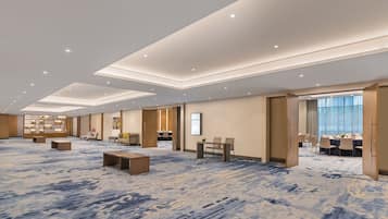 A spacious hotel lobby with a patterned carpet, seating areas, a reception desk, and a large window with curtains.