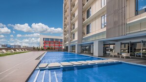 A modern hotel with a large outdoor swimming pool, lounge chairs, and a clear view of the surrounding buildings. - Citadines Bay City Manila (Pasay)