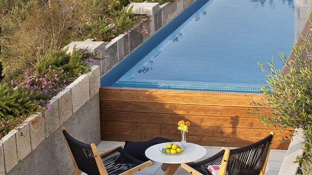 A swimming pool with two chairs and a table, overlooking a historic cityscape.