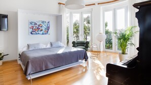 A modern bedroom with a bed, a green armchair, a piano, and large windows.
