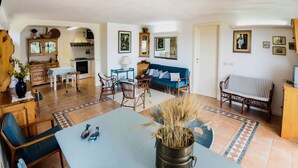 A cozy living room with a sofa, chairs, a dining table, and a kitchen area. - Dream holidays in Sardinia! (Chia)