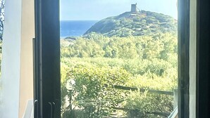 A room with a sliding glass door leading to a terrace with a view of a hilly landscape and the sea. - Dream holidays in Sardinia! (Chia)