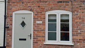 Una casa de ladrillo con una puerta blanca identificada con el número 16, una ventana pequeña y un letrero que dice 'BELL COTTAGE'.