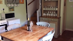 Un comedor con una mesa de madera, sillas blancas, una botella de vino y una copa de vino. Una lámpara colgante naranja ilumina la mesa.