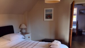 Una cama bien hecha con sábanas blancas y toallas enrolladas, una lámpara de noche y un cuadro en la pared.